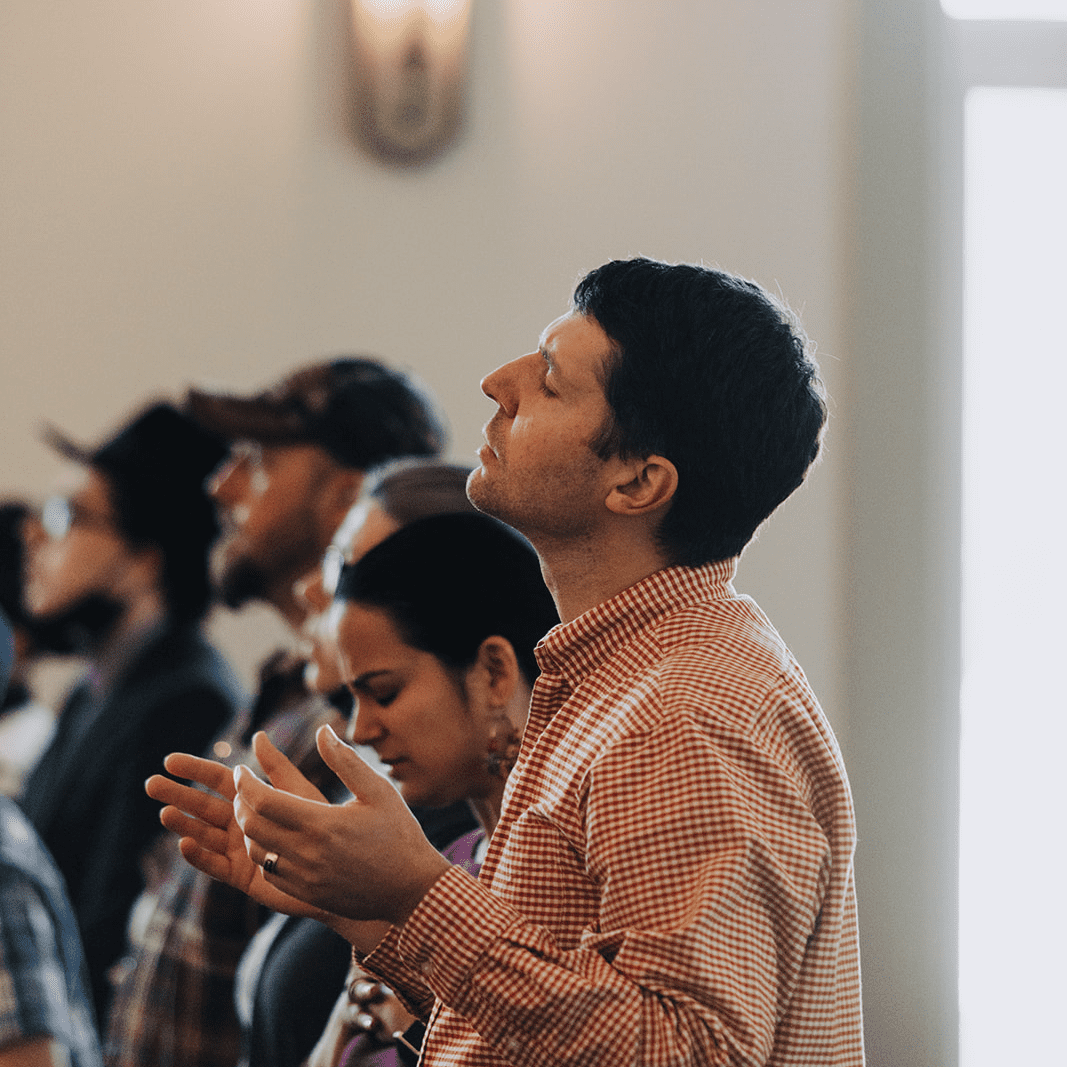 Devoted churchgoer praying with closed eyes and raised hands during a worship service at Anderson Hills Church Salem