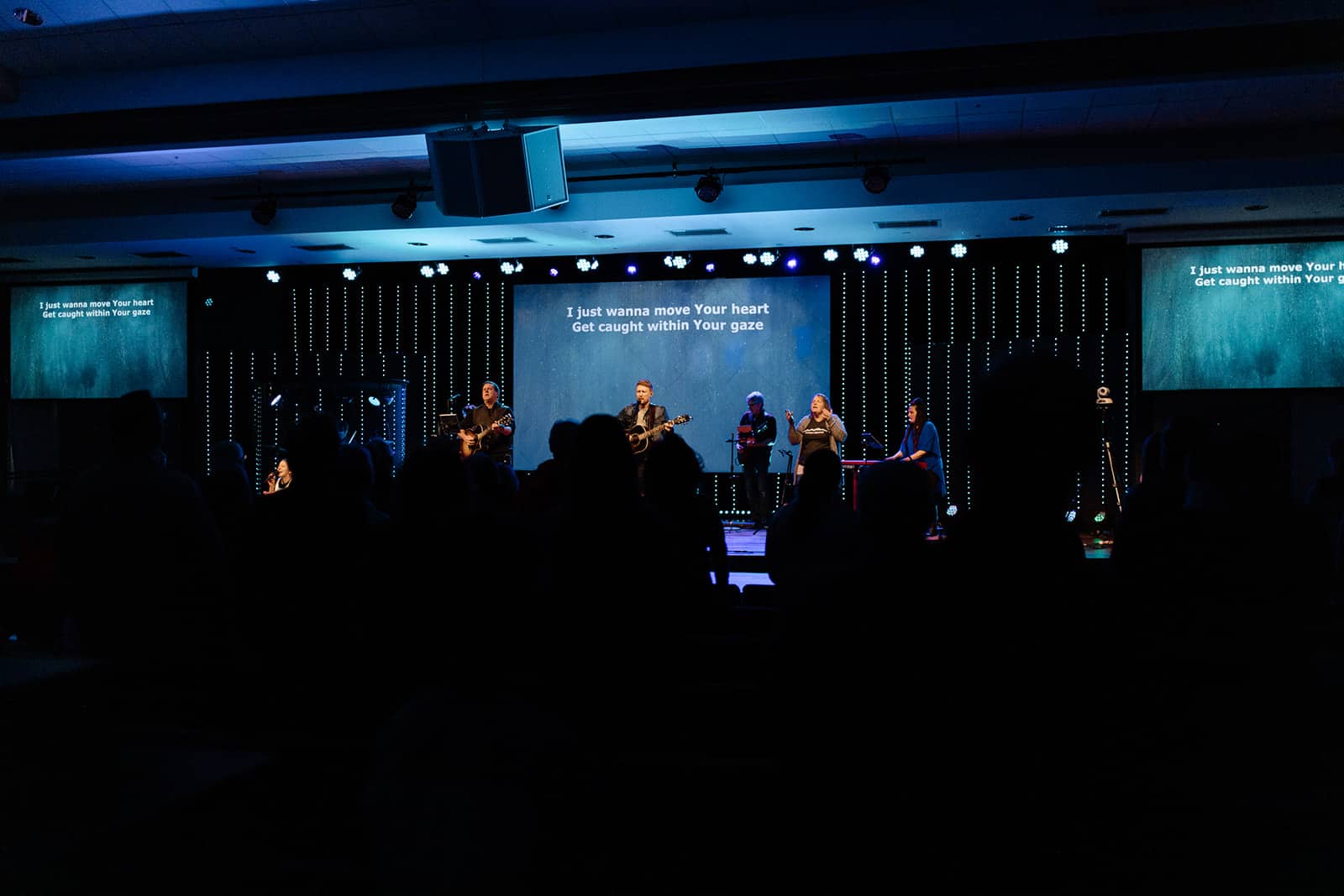 Worship band performing contemporary Christian music under blue stage lights at Anderson Hills Church, within an immersive worship experience with lyrics projected on the screen for the congregation.