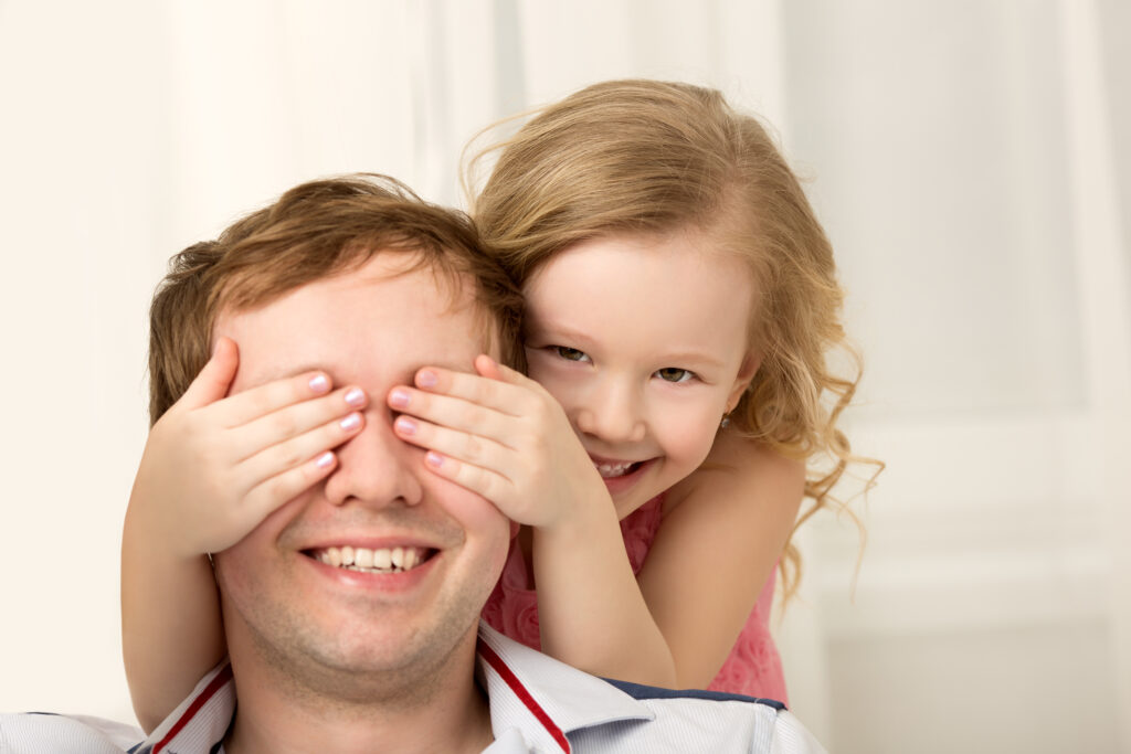 Father and daughter playing at home. Little girl closing dads eyes with hands and laughing. Family fun together
