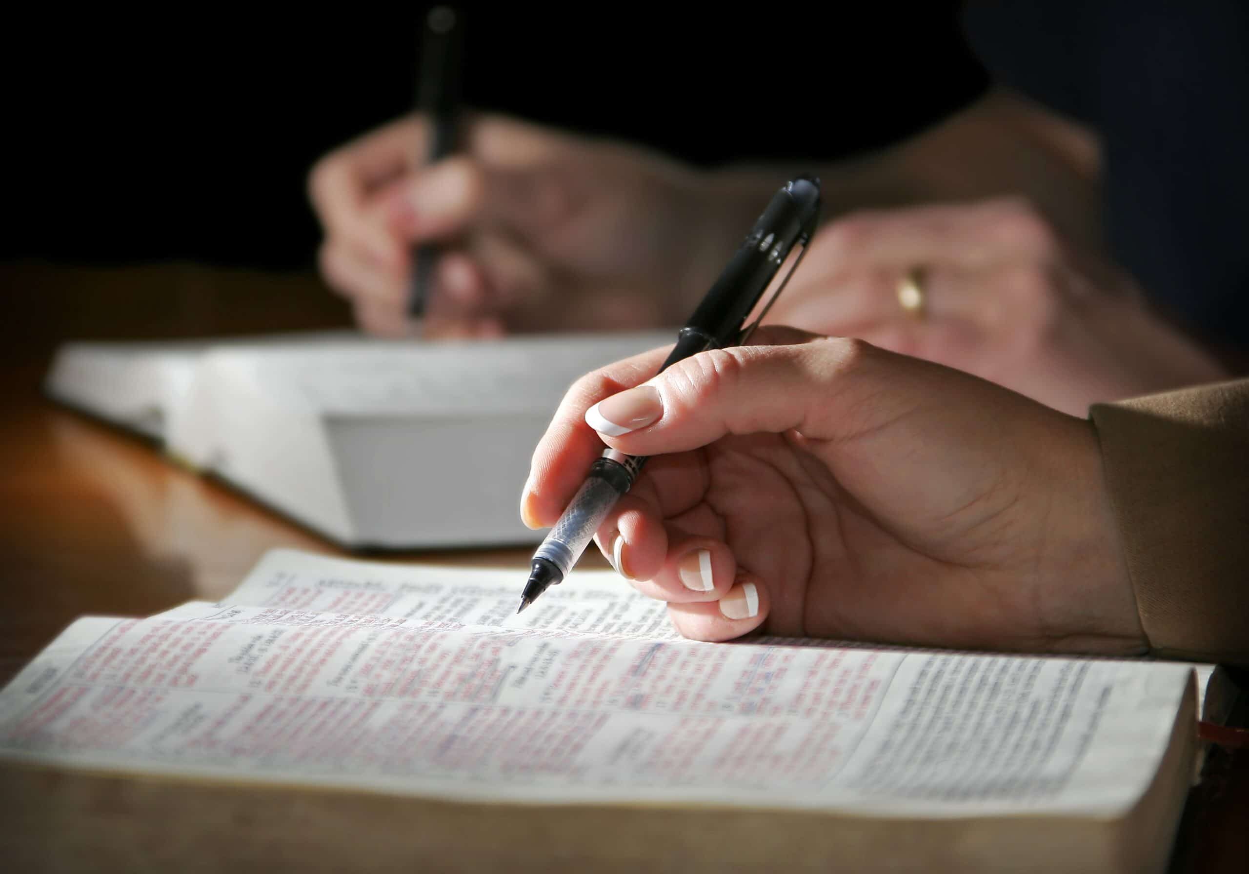 The hands of a couple are highlighted as they study the Holy Bible together - focus point on the woman's foreground hand.
